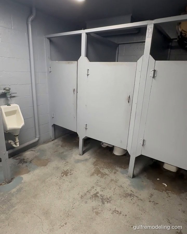 Commercial restroom before the remodel: worn concrete floor and old stalls
