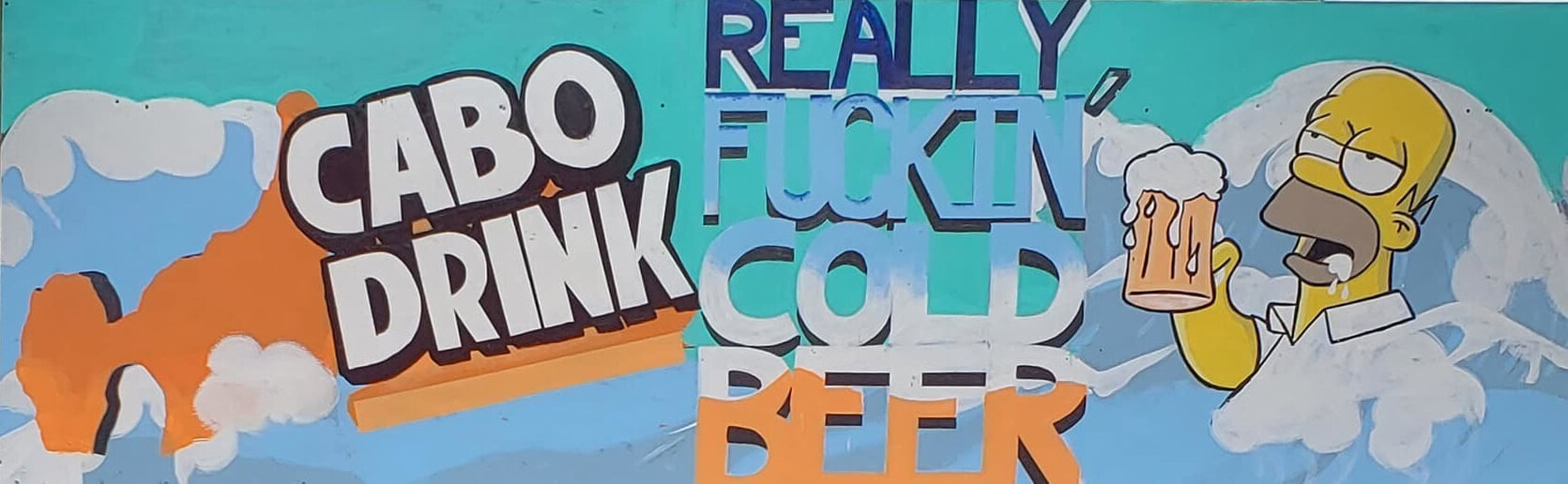 Photo of the sign in front of Cabo Drink Restaurant and Bar in Cabo San Lucas with Homer Simpson Drinking a beer and the Cabo Arch and the words Really Fuckin Cold Beer