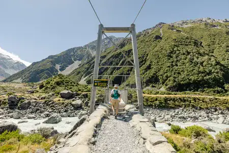 One step closer to Aoraki — first swing bridge on the Hooker Valley Track. © Anna Jackowska Male hiker with a backpack, viewed from behind, stepping onto the first swing bridge on the Hooker Valley Track in New Zealand’s Southern Alps.