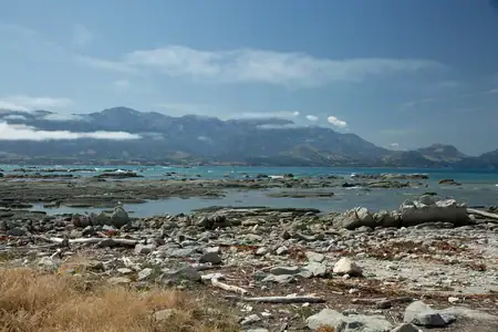 The stunning meeting of mountains and sea along the Kaikoura coast. Rocky Kaikoura beach and turquoise sea with the cloudy Seaward Kaikoura Range in the background.