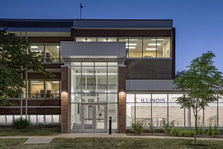 Modern Illinois building with glass entrance and brick facade, surrounded by landscaped greenery.