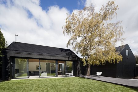 Modern minimalist black house with floor-to-ceiling windows and wooden deck. Autumn foliage.