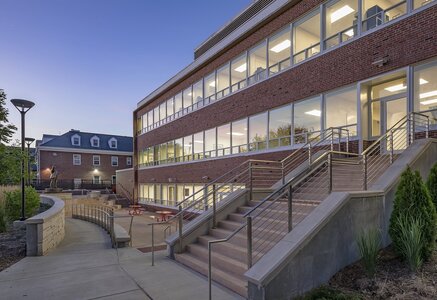 Modern red brick building with accessible entrance and well-lit pathway during early evening.