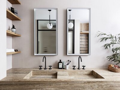 Modern double sink bathroom with natural stone countertop, black fixtures, floating shelves, and green plant.