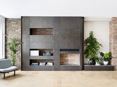 Modern industrial living room with grey sliding door, exposed brick shelves, and lush green plants.