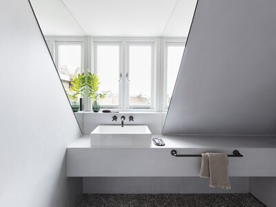 Modern minimalist bathroom with angular sink, chrome faucets, natural light, and potted plants.