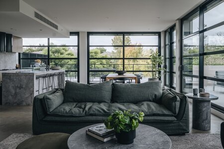 Modern open-concept living space with green sofa, large windows, and minimalist kitchen.