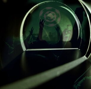 Green neon tunnel frames silhouetted concert crowd with raised hands and a glowing symbol.