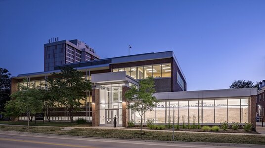 Modern university building at twilight with glass façade and warm interior lighting.
