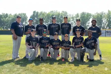 A youth baseball team in navy uniforms poses for a group photo on a sunny field, with two coaches standing on each end and players kneeling and standing in two rows—representing the teamwork and camaraderie fostered at Telos Academy. at Telos