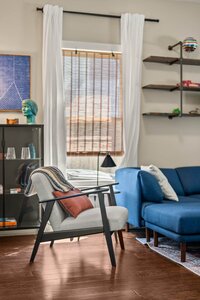 Bright living room with armchair, blue sofa, window blinds, and decorative accents.