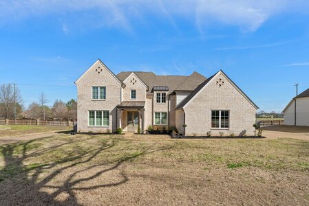 Elegant brick home featuring large windows and landscaped front yard.