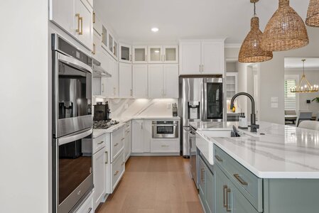 High-resolution image of a contemporary white and gray kitchen with marble countertops and stainless steel appliances.