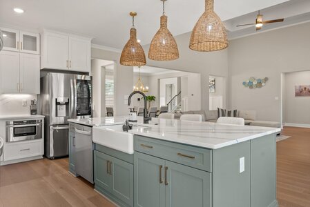 Spacious, contemporary kitchen featuring a large island, white cabinets, and woven pendant lights.