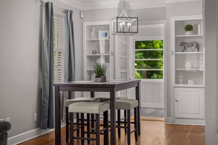 Bright dining area with large window, white walls, gray curtains, and wooden table.