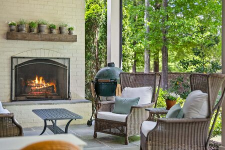 Charming outdoor seating area featuring a fireplace, wicker chairs, and lush garden view.