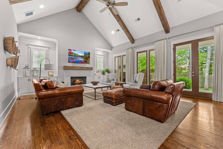Stylish living room with leather furniture, fireplace, and expansive windows overlooking a lush backyard. Ideal for home comfort.