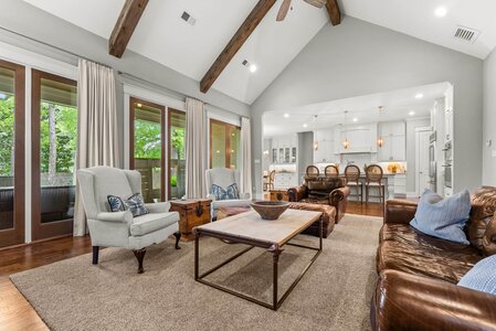 Bright, open-concept living space featuring vaulted ceilings, wooden beams, and large windows bringing in natural light.