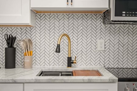 Elegant kitchen with gold faucet, white marble countertop, and geometric tile backsplash, showcasing sleek design.