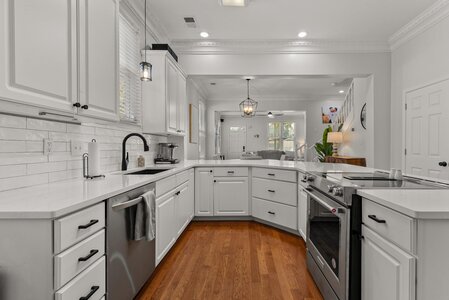 Bright modern kitchen with white cabinetry, stainless steel appliances, and hardwood flooring.