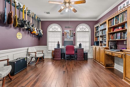 Guitar wall display and home office setup with musical instruments and books.