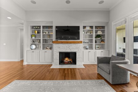 Elegant living room featuring a cozy fireplace, TV, white shelving, and bright windows.