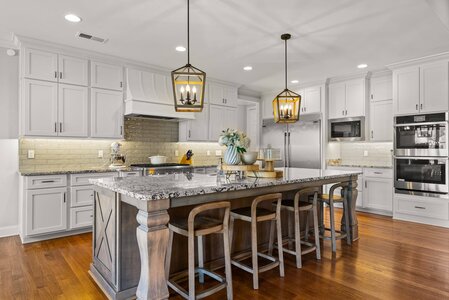 Bright, stylish kitchen featuring white cabinets, granite island, and elegant pendant lights.