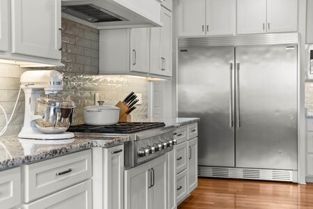 Stainless steel refrigerator and matching oven in a stylish modern kitchen with white custom cabinetry.