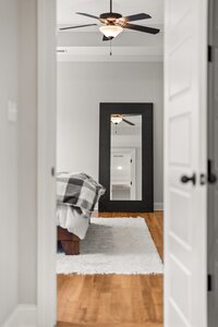High-quality image of a bedroom seen through a doorway, showcasing a ceiling fan, mirror, and cozy bedding.