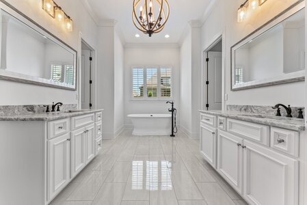 Bright bathroom featuring double vanities with marble countertops and a vintage clawfoot tub under a window.
