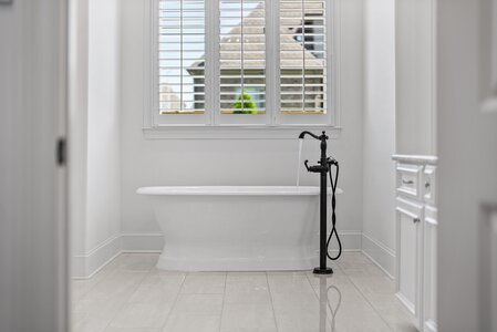Luxurious white freestanding bathtub with vintage-style black faucet and window shutters, creating a sophisticated bathroom ambiance.