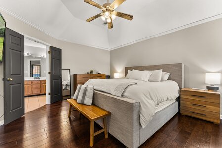 Cozy bedroom with neutral tones, wooden furniture, and soft lighting, featuring a large comfy bed and access to private bathroom.