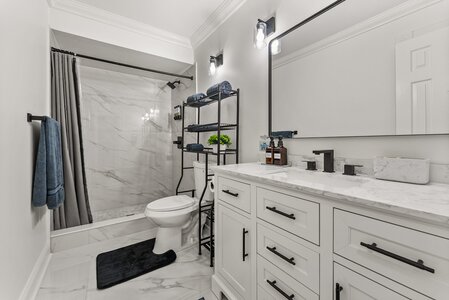 Luxurious white bathroom featuring a marble countertop, black fixtures, and organized shelving, perfect for upscale home design.