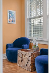Comfortable living room with blue velvet armchairs, wooden side table, and artwork on warm wall.