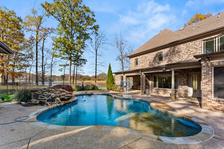 Spacious backyard with swimming pool, waterfall, and scenic lake view in a private home.