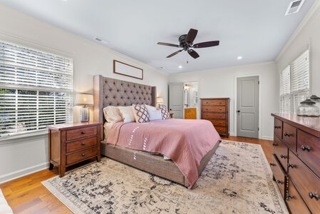 Bright bedroom featuring wooden nightstands, dressers, and a plush upholstered bed with decorative pillows.