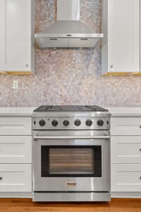 Alt: Modern stainless steel gas stove with black knobs and oven, kitchen backsplash in tile pattern.