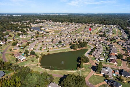 Aerial view of a suburban neighborhood featuring a central pond, lush landscaping, and various homes, ideal for real estate insights.