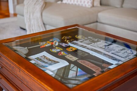 ALT: Glass-topped display case showing military patches, photos, and souvenirs in a cozy home setting.