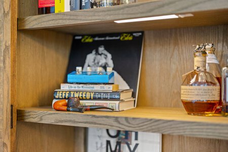 Close-up of books, whiskey bottles, and smoking pipe on wooden bookshelf.