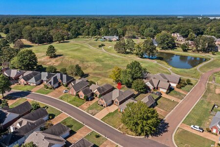 Aerial view of a residential property near a golf course and pond, highlighting luxury homes and scenic landscapes.