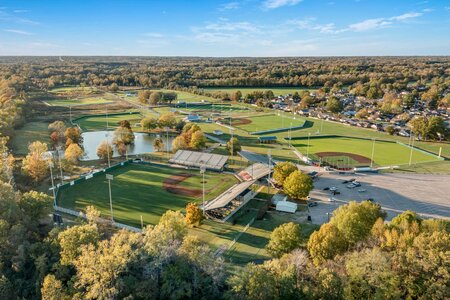 Aerial view of a sports complex featuring baseball fields, parking, and scenic greenery with trees and a pond.
