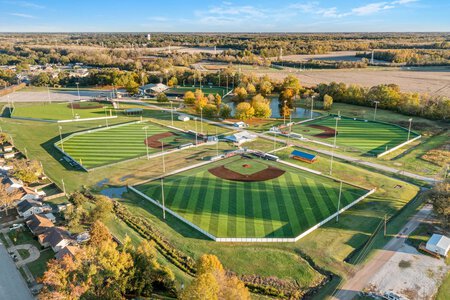 Aerial view of a baseball complex with multiple fields, lush greenery, and surrounding nature.