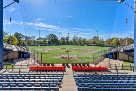 Baseball stadium with seating, netting, and view of lush trees and blue sky.