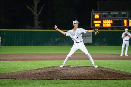 Baseball pitcher throwing a pitch on the mound during a night game, focused on the strike zone.