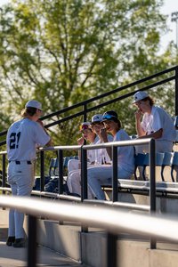 Young baseball players sitting and discussing in dugout with trees background.