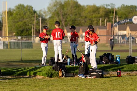 Young boys in red uniforms preparing for baseball game on field.