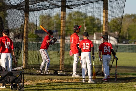 Young baseball players in uniform practicing hitting in batting cage during game or practice.