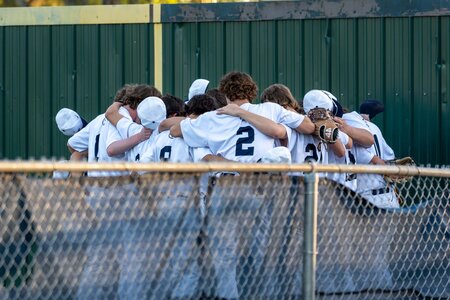 Baseball players in white uniforms embrace in team huddle on the field.