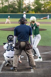 Baseball batter swinging at a pitch with catcher and umpire behind him.